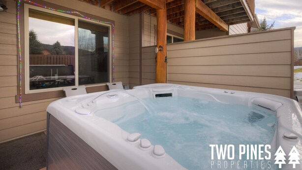Een hottub in een openluchtsetting, met houten balken erboven en een raam met uitzicht op een achtertuin.