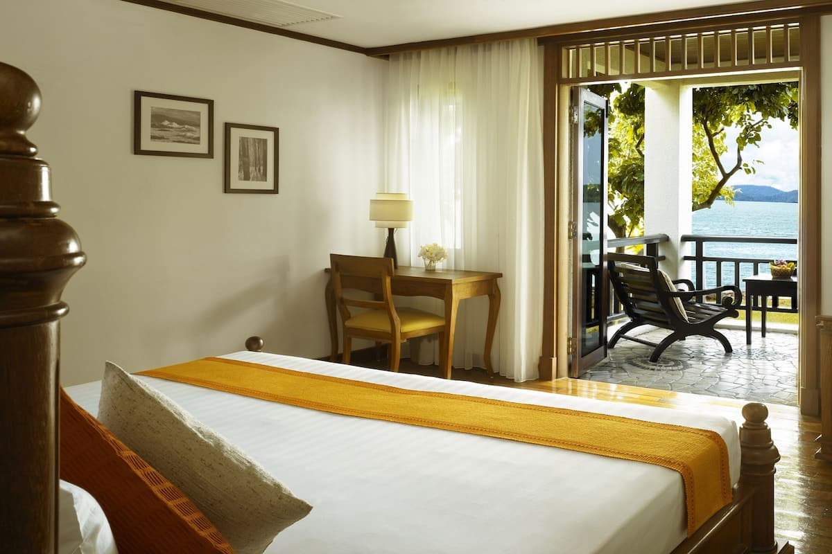 A hotel room with a bed, a desk with a chair, a small table with a lamp, and a view of the outdoors.