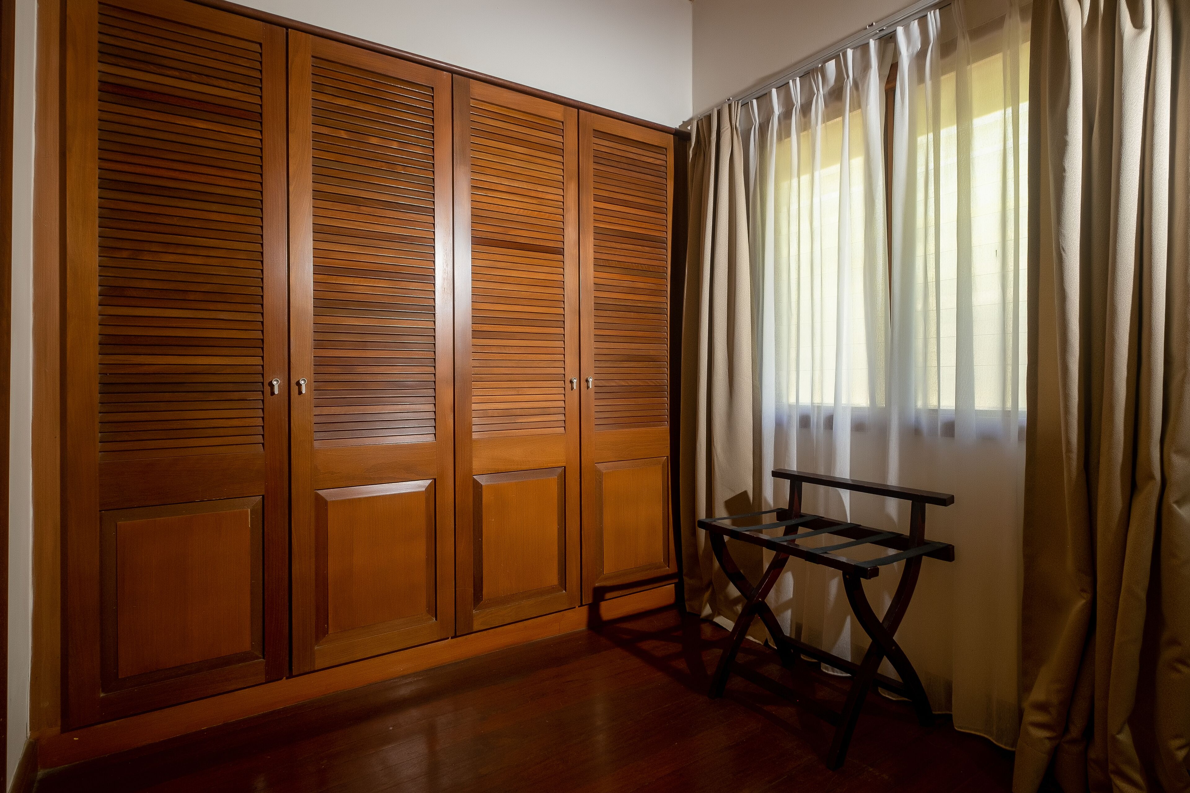 Una habitación con un armario de madera, una mesita y una ventana con cortinas.