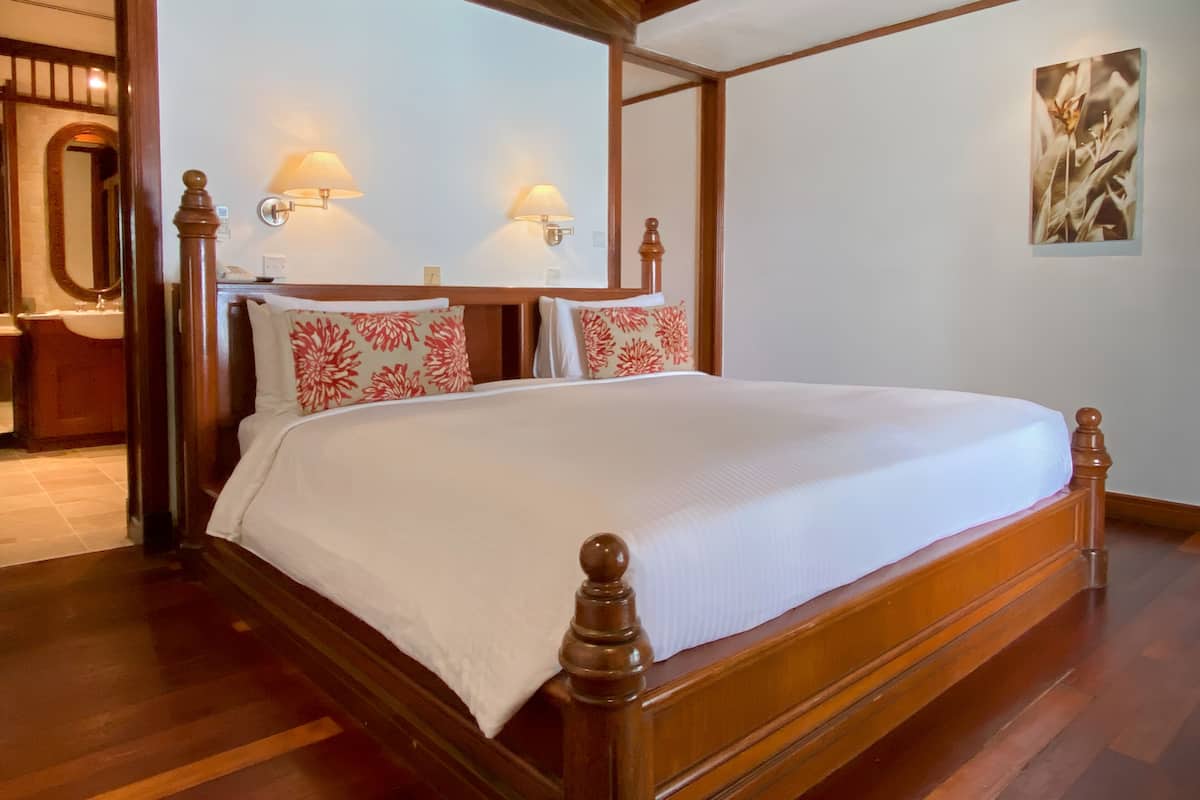 A large, wooden-framed bed with white bedding, two wall-mounted lamps, and a painting on the wall.