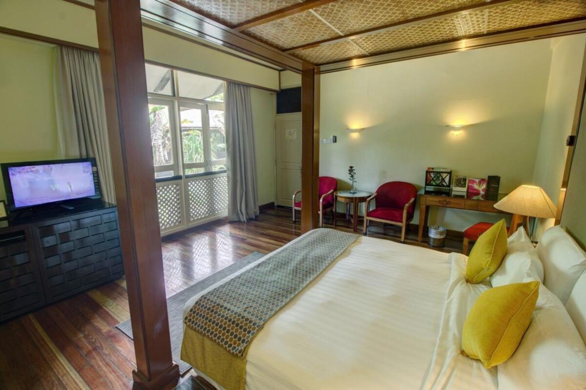 A hotel room with a large bed, a television, a desk with a chair, and a view of the outdoors.