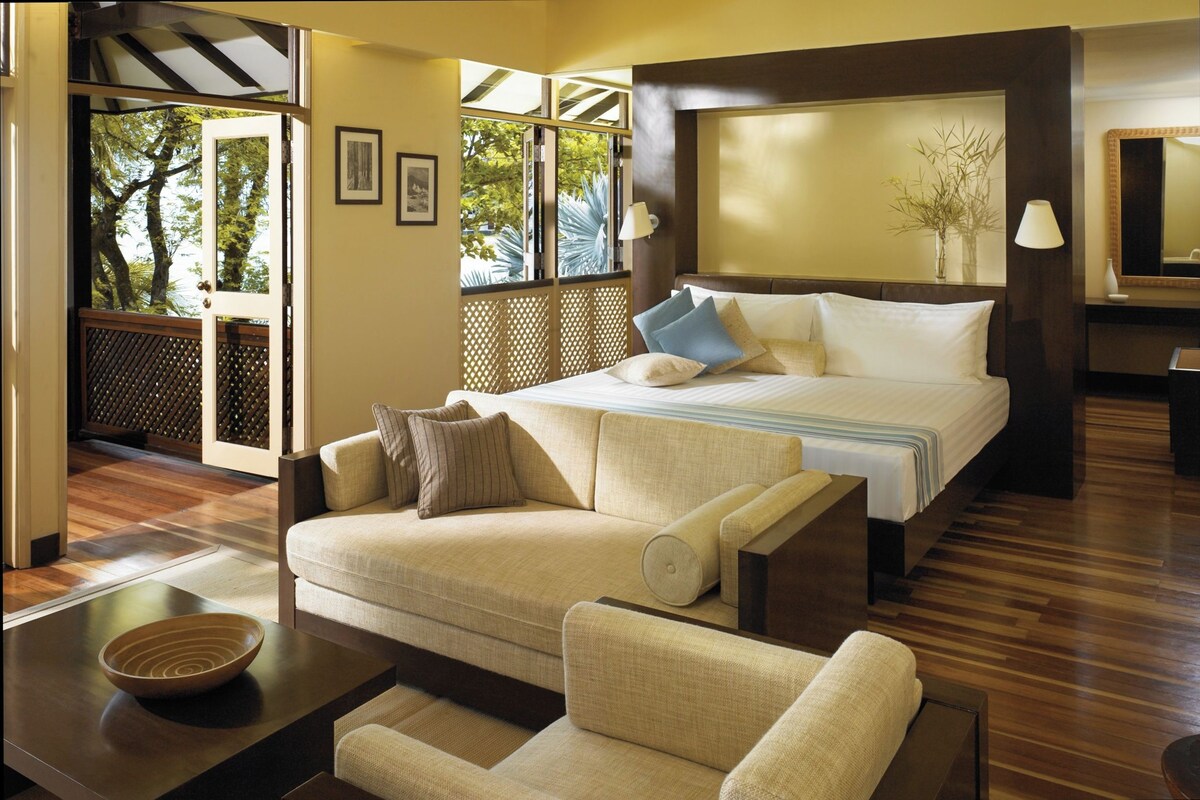 A hotel room with a bed, a sofa, a coffee table, and a view of trees through a window.