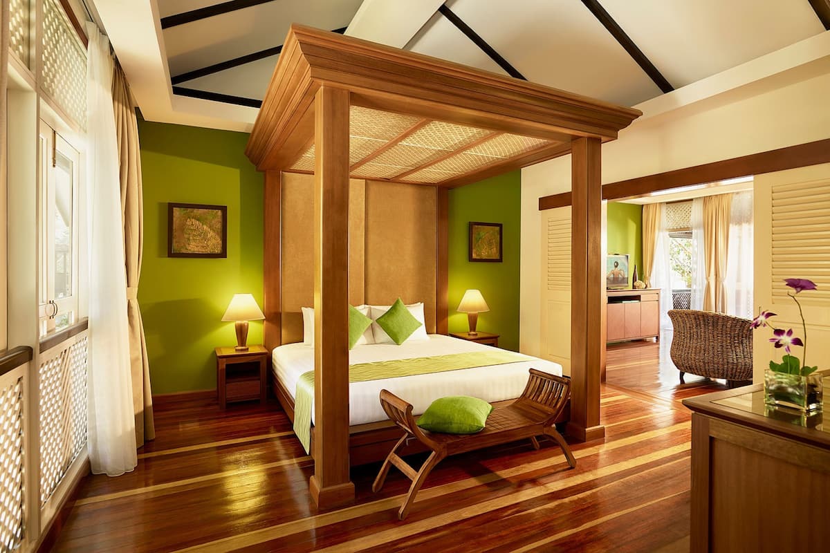 A room with a four-poster bed, wooden flooring, green walls, and a wicker chair.