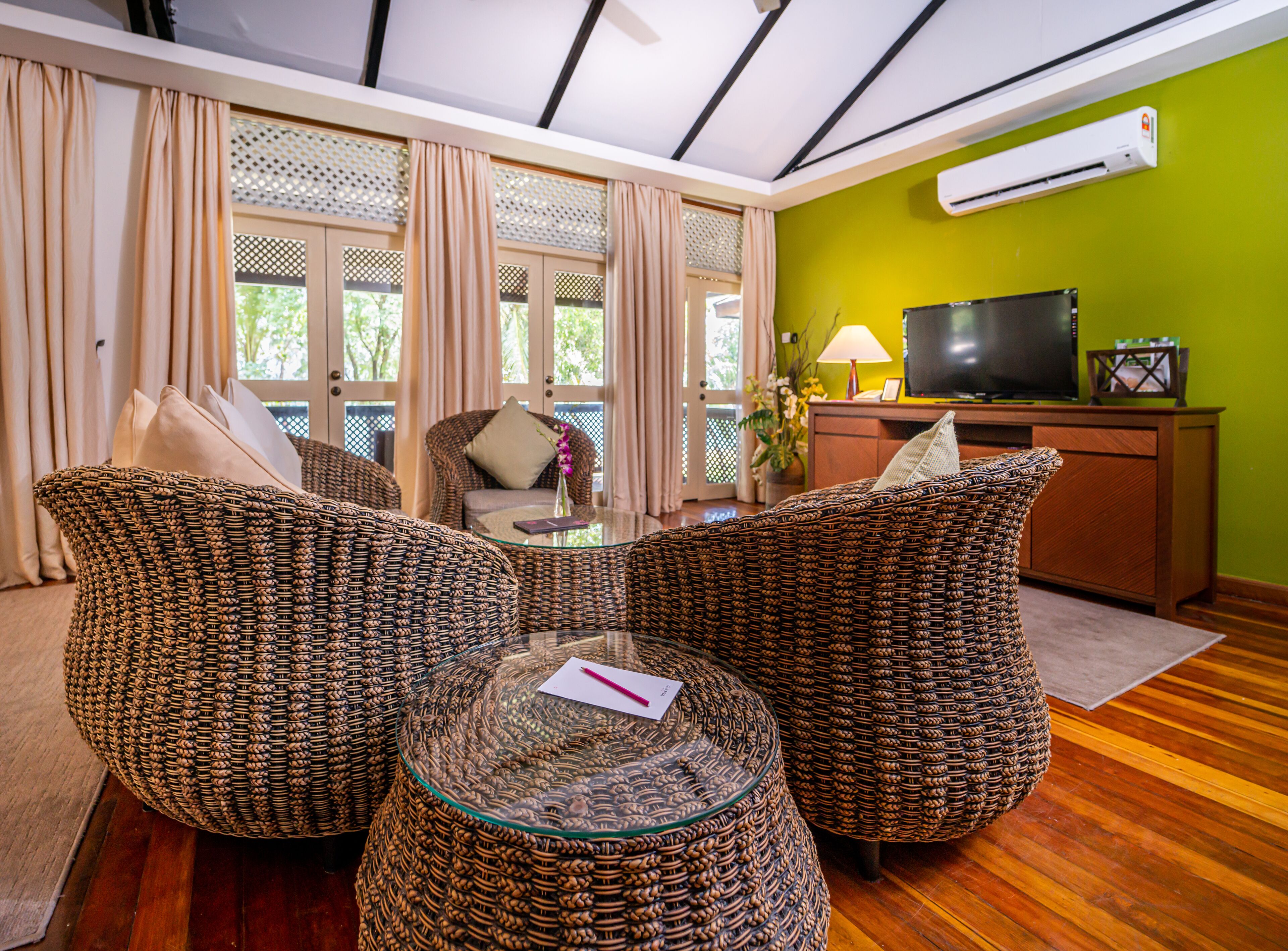 A living room with wicker furniture, a glass coffee table, a television, and a green wall.