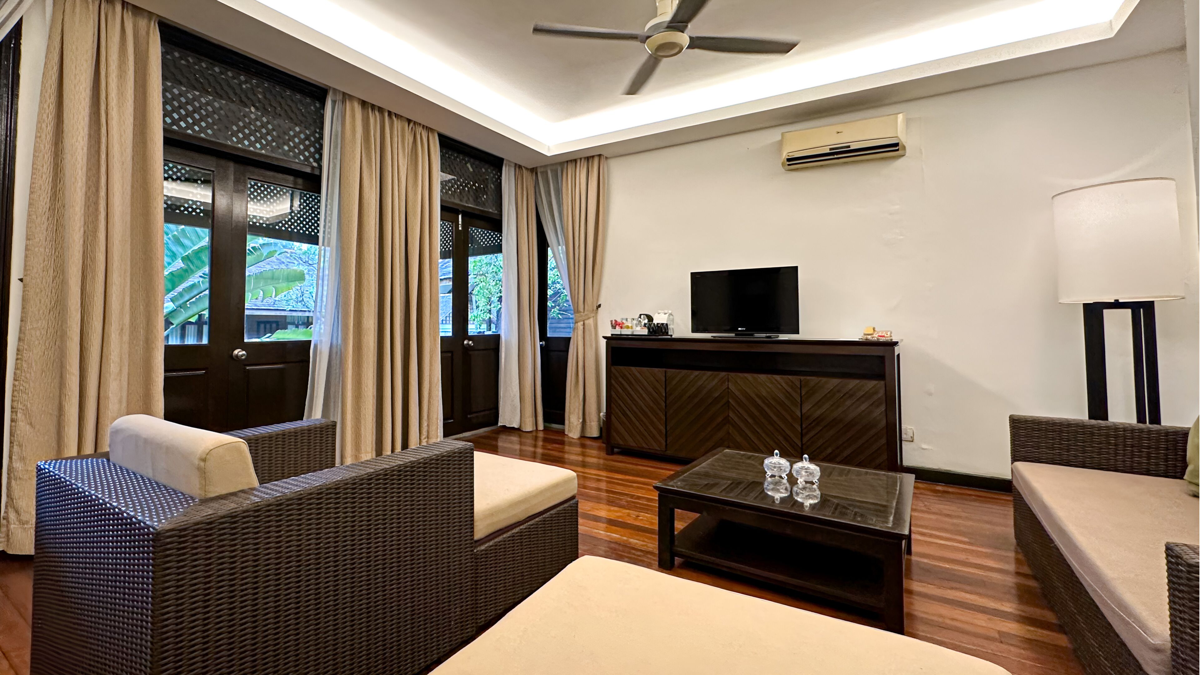 A modern living room with wicker furniture, a flat-screen TV, and a ceiling fan.