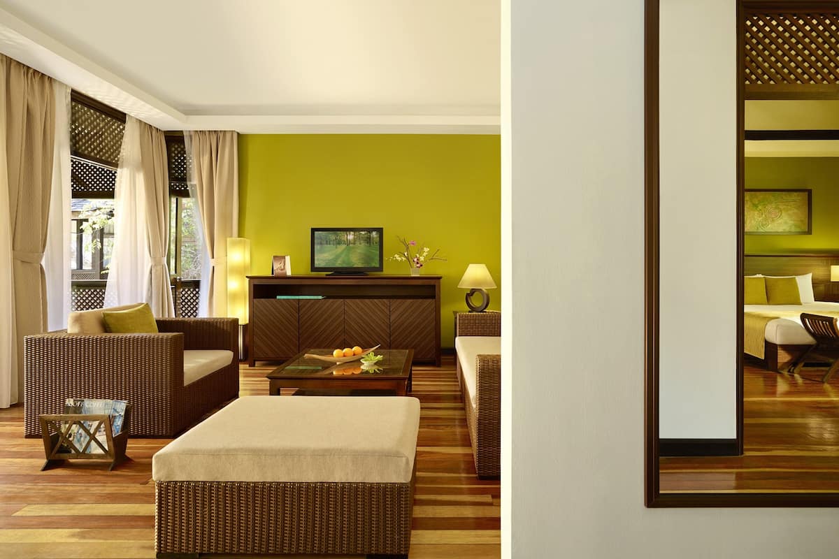 A hotel room with a green wall, a television, a sofa, a coffee table, and a bed.