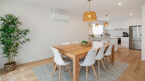 Een moderne keuken met witte kasten, een roestvrijstalen koelkast en een eethoek met een houten tafel en witte stoelen.