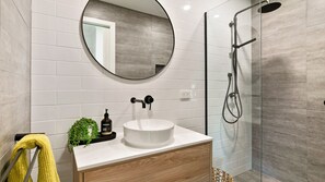 Een moderne badkamer met een ronde spiegel, een wit wastafelmeubel en een douche met glazen wanden.