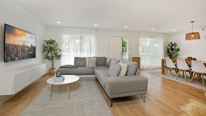 A modern living room with a grey sectional sofa, a round coffee table, and a dining area with a wooden table and white chairs. - Lansell Retreat in Cowes (Cowes)
