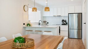 A modern kitchen with white cabinetry, a stainless steel refrigerator, and a central island with bar stools. - Lansell Retreat in Cowes (Cowes)