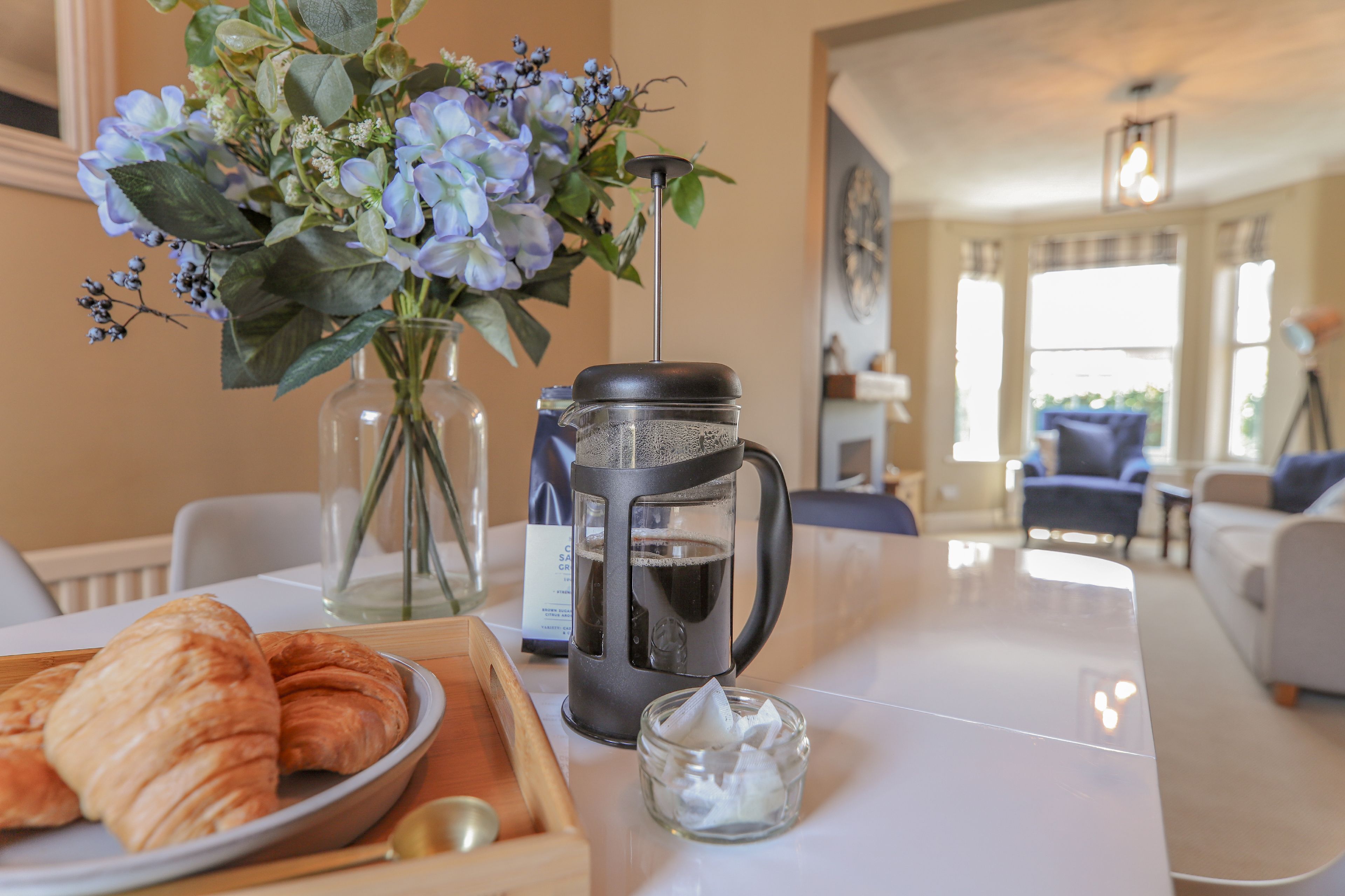 Une table de petit-déjeuner avec des croissants, une machine à café et un vase de fleurs.