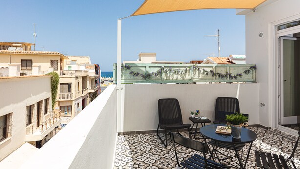 Ein Balkon mit zwei Stühlen und einem kleinen Tisch, mit Blick auf eine Stadtlandschaft mit Gebäuden und blauem Himmel.