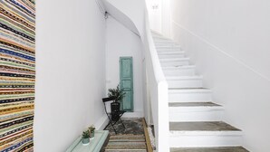 Ein schmaler Flur mit einer weißen Treppe, einer grünen Tür und einem farbenfrohen Teppich.