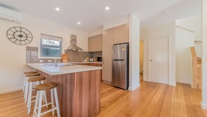 Une cuisine moderne dotée d’un îlot central, de tabourets en bois, d’appareils électroménagers en acier inoxydable et d’une grande horloge murale.