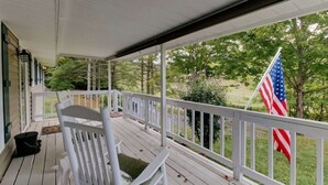 A covered porch with white railings, a white rocking chair, and an American flag. - PET FRIENDLY COTTAGE 3.5 MILES FROM LAKE MOOMAW! (Hot Springs)