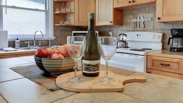 A kitchen with wooden cabinets, a white stove, and a bowl of fruit on the counter. - PET FRIENDLY COTTAGE 3.5 MILES FROM LAKE MOOMAW! (Hot Springs)