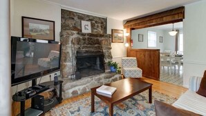 A living room with a stone fireplace, a television, a coffee table, and a patterned rug. - PET FRIENDLY COTTAGE 3.5 MILES FROM LAKE MOOMAW! (Hot Springs)