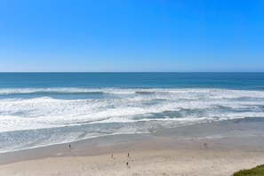 A beach with people walking along the shore and waves crashing onto the sand.