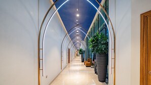 Ein moderner Hotelkorridor mit gewölbter Decke, großen Kübelpflanzen und einer Holztür auf der rechten Seite.