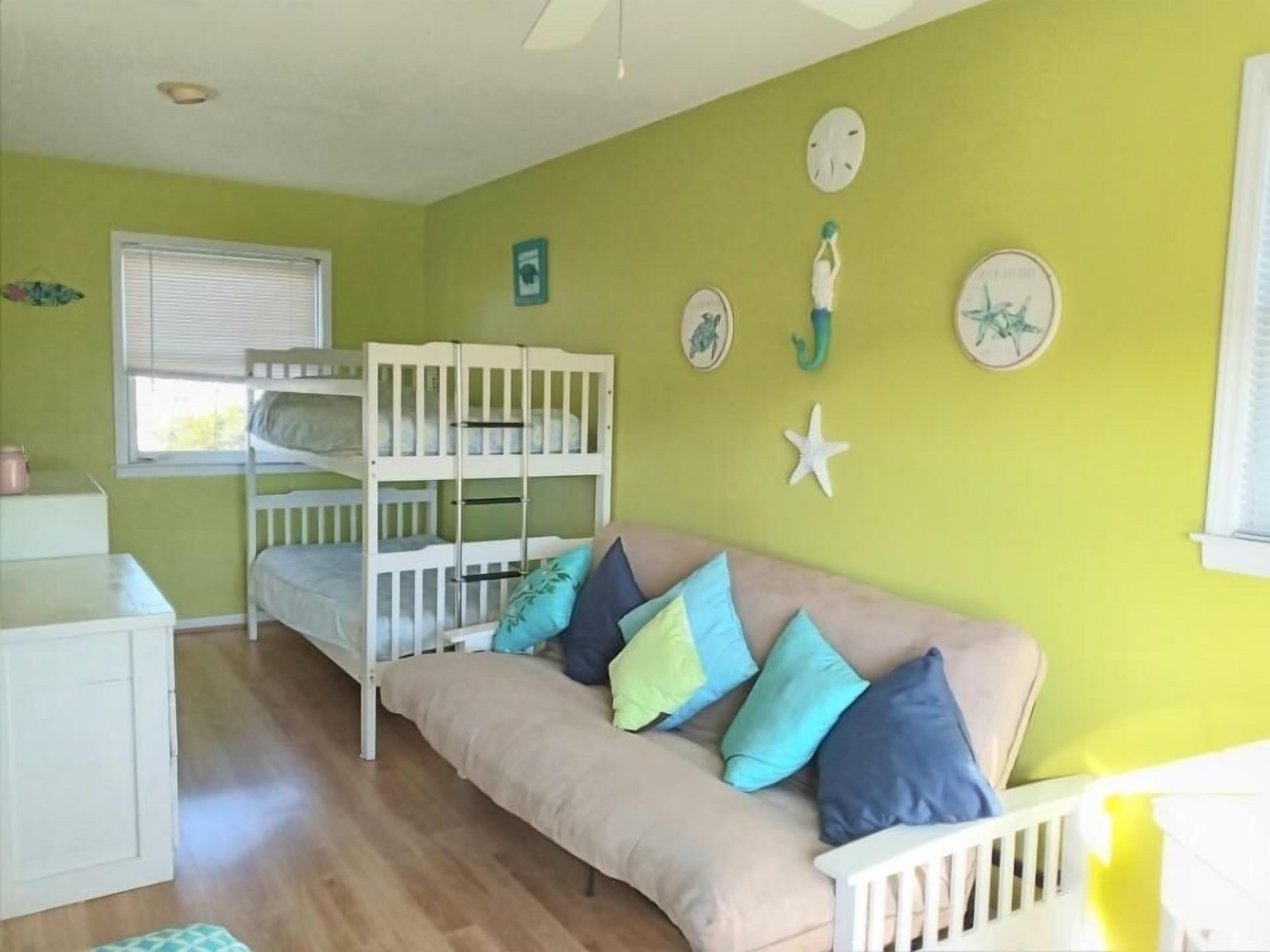 A room with bunk beds, a sofa, and a window with blinds.