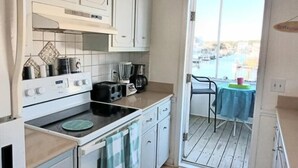 A compact kitchen with white cabinets, a stove, and a toaster. A balcony with a table and chairs is visible through an open door. - 1 Galway Girl 3 Bedroom Home by RedAwning (Supply)