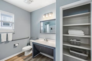 A bathroom with a toilet, sink, mirror, towel rack, and storage shelves.