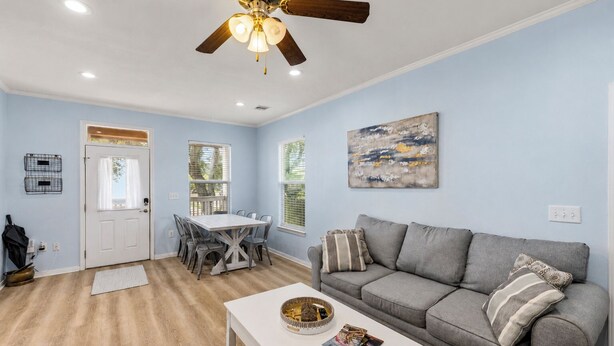 A living room with a gray sofa, a white coffee table, a dining table with chairs, a ceiling fan, and a painting on the wall. - Summer Bliss | Walk to Beach • Master Suite • Bunk Beds • Sleeps 9 (Galveston)
