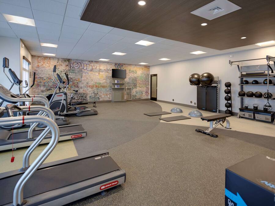 A gym with treadmills, elliptical machines, a wall-mounted TV, and various exercise equipment.