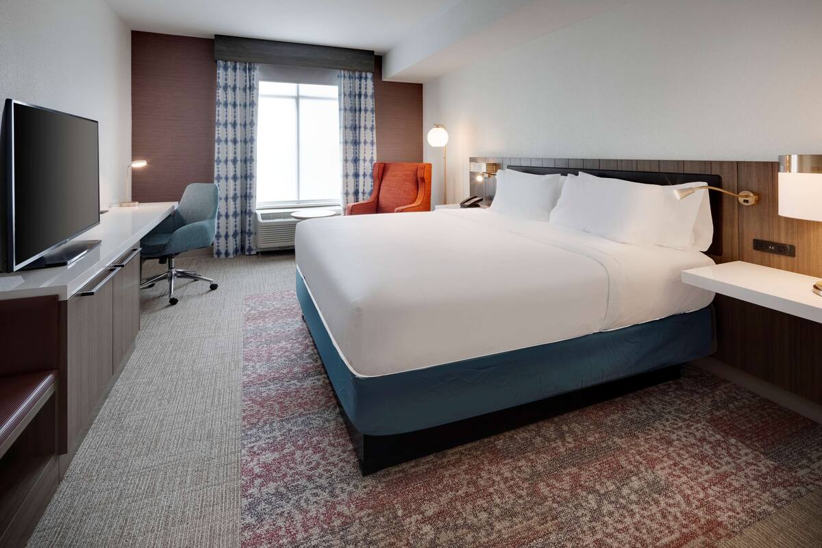 Una habitación de hotel con una cama grande, televisión, escritorio y una silla.