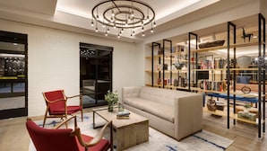 Un salon moderne avec un canapé, des fauteuils rouges, une table basse et une bibliothèque contenant divers objets.