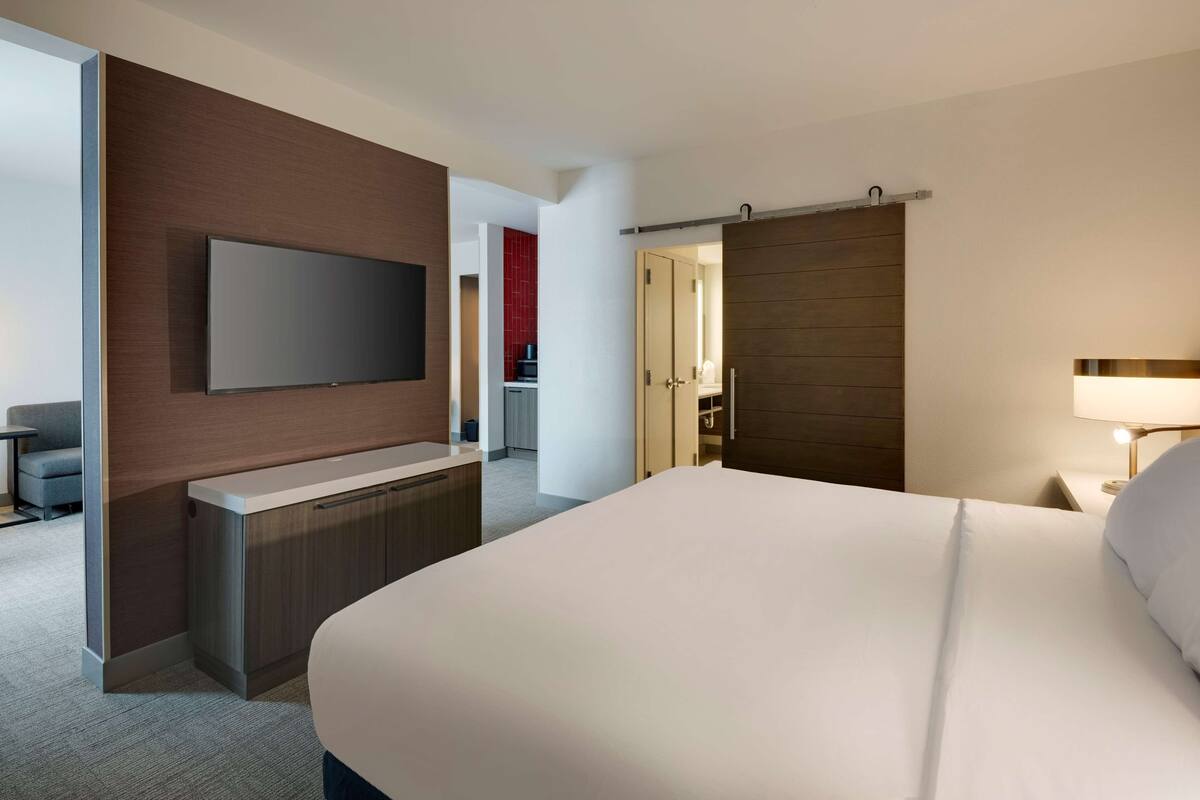 Habitación de hotel con una cama grande, un televisor de pantalla plana en la pared, un escritorio con una silla y un armario con puerta corredera.