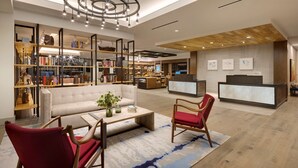 Un hall d’hôtel moderne doté d’un espace salon central, d’un comptoir d’accueil et d’une bibliothèque remplie de livres.
