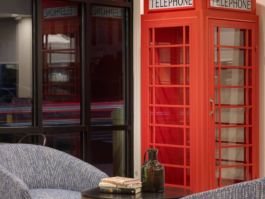 Ein Zimmer mit zwei blauen Polstersesseln, einem kleinen runden Tisch und zwei roten Telefonkabinen.