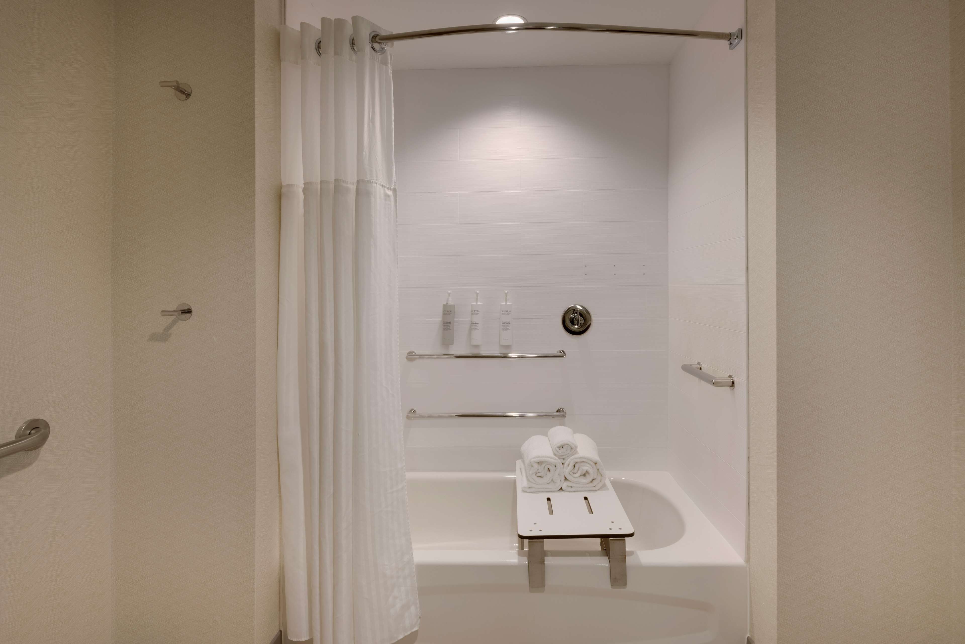 Une salle de bain moderne avec une baignoire, un espace douche et une petite table avec des serviettes.