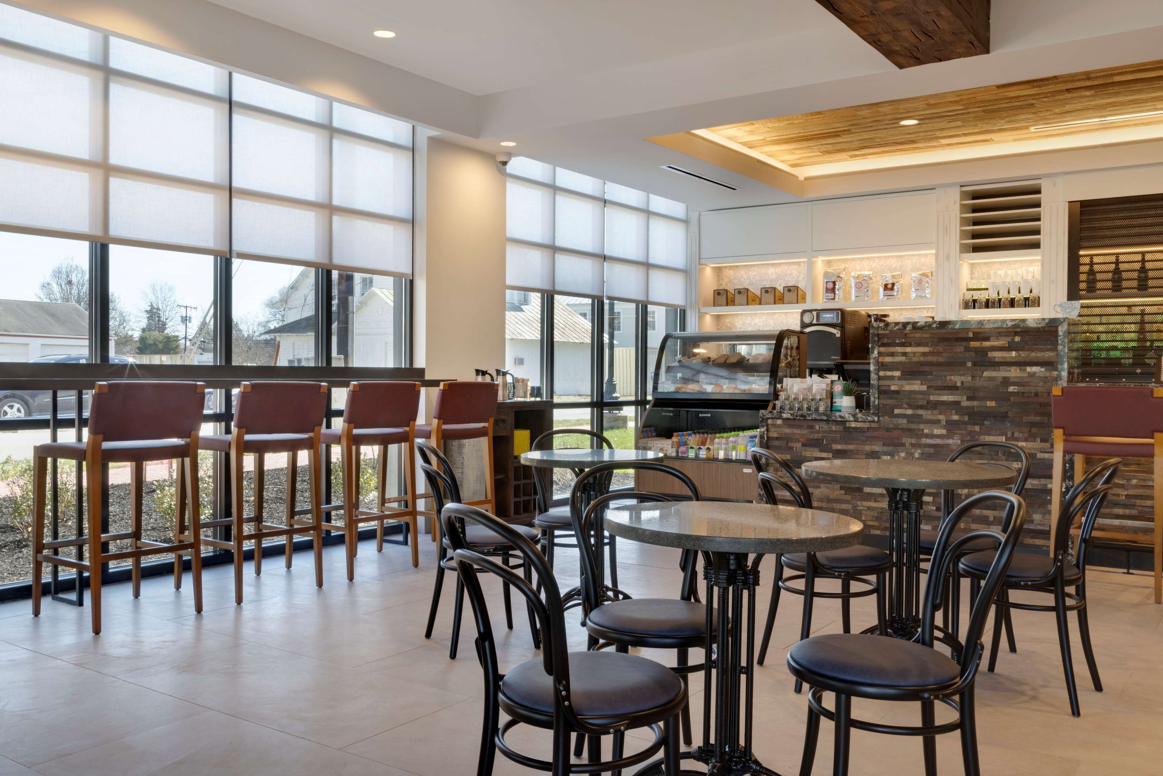 A modern restaurant with large windows, a stone fireplace, and a variety of seating options including round tables and bar stools.