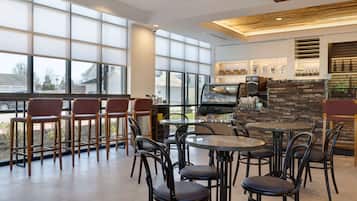 A modern restaurant with large windows, a stone fireplace, and a variety of seating options including round tables and bar stools.