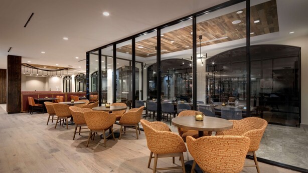 Un espace repas moderne avec des tables rondes et des chaises en osier, de grandes fenêtres et un plafond en bois.