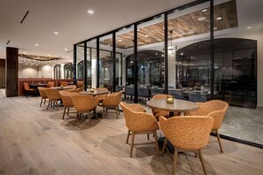 Un espace repas moderne avec des tables rondes et des chaises en osier, de grandes fenêtres et un plafond en bois.