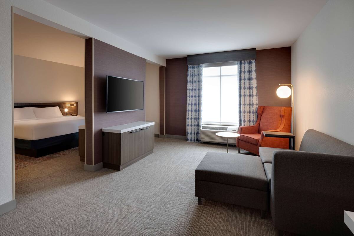 Habitación de hotel con cama, televisor, escritorio, silla y sofá.