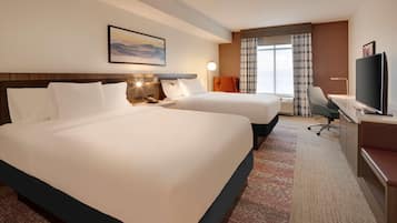 Habitación de hotel con dos camas grandes, un escritorio con silla, un televisor y una ventana con cortinas.