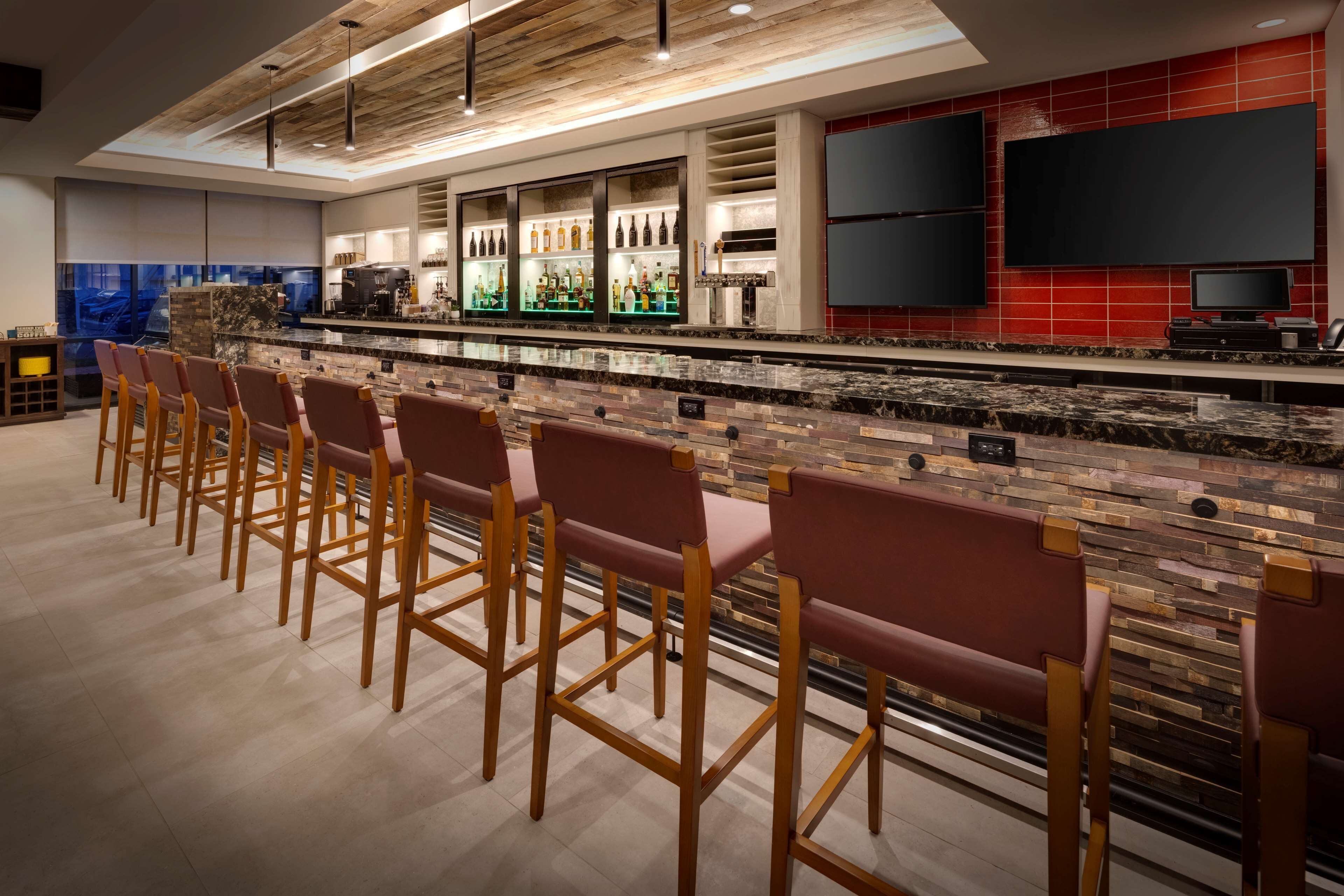 A bar area with a long counter, multiple bar stools, and a television screen mounted on the wall.