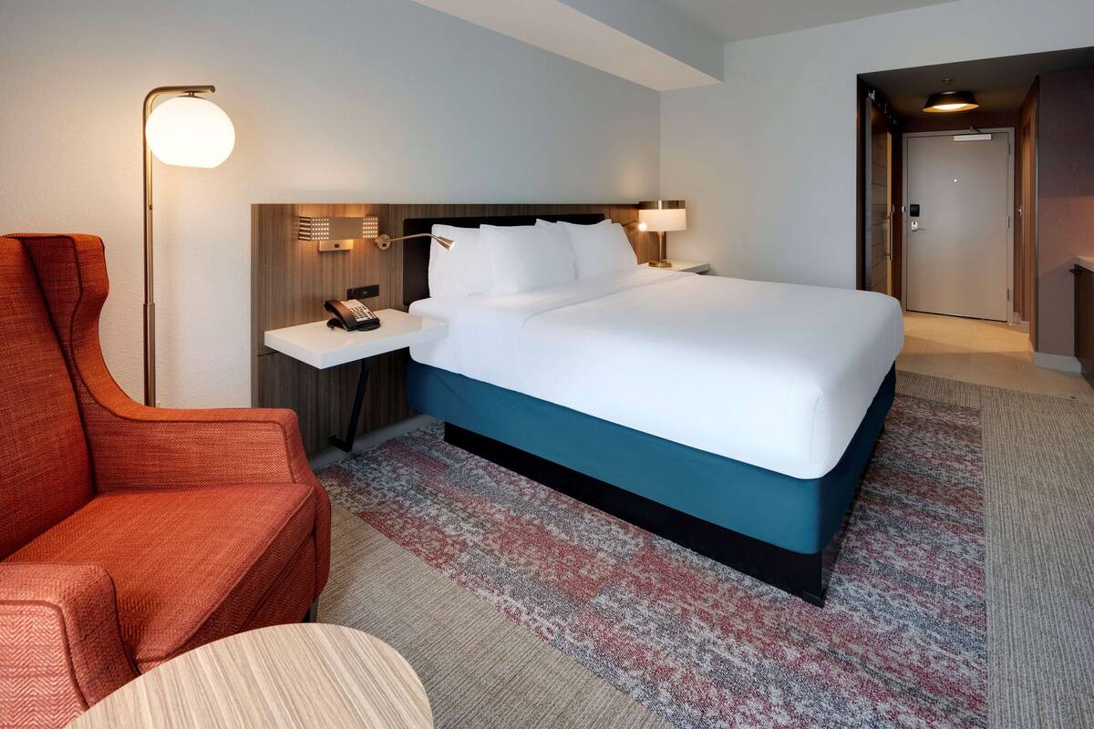 Una habitación de hotel con una cama grande, un escritorio con teléfono, una silla y una lámpara.