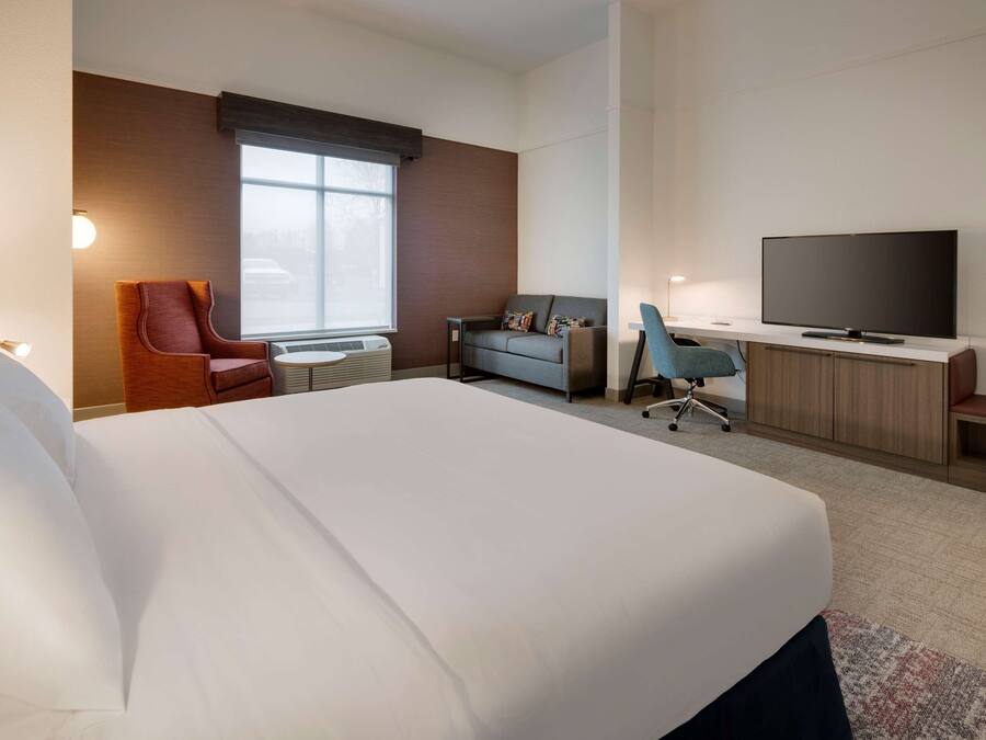 Una habitación de hotel con una cama grande, un sofá, un escritorio con televisor y una silla.