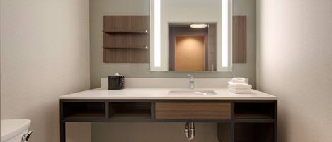 A modern bathroom with a white sink, a mirror with integrated lighting, a towel rack, and a toilet.