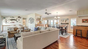 A spacious living area with a large sofa, dining table, and chairs, a kitchen in the background, and a ceiling fan.