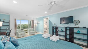 Un dormitorio con una cama grande, un ventilador de techo, un televisor y vistas al exterior.