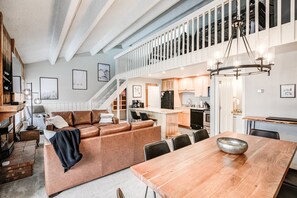 A spacious living area with a wooden dining table, a brown leather sofa, and a staircase leading to an upper level. - Lift Condo: Walk To Slopes, Downtown (Breckenridge)