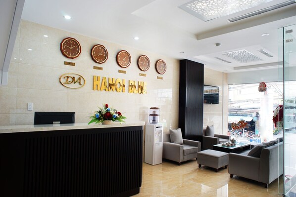A hotel reception area with a modern design, featuring a reception desk, seating area, and clocks displaying times from various cities.