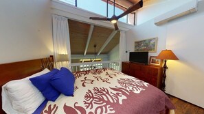Un dormitorio con cama, televisor, lámpara y un cuadro en la pared.