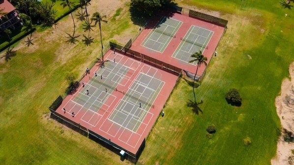 Eine Vogelperspektive eines Tennisplatzkomplexes mit mehreren Plätzen, umgeben von Rasen und Palmen.